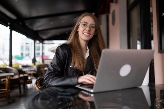young stylish woman sits on the stairs next to a popular cafe with a cup of coffee and watches a mobile phone.