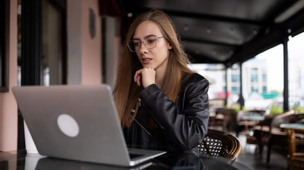 young woman working online on laptop in city cafe.