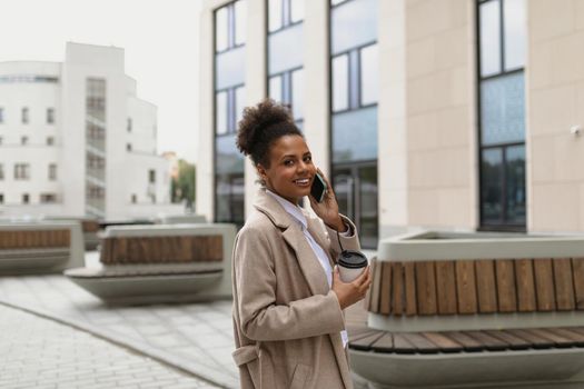 african american young woman talking on a mobile phone next to a business center with a smile on her face.