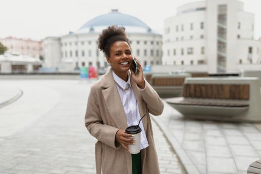 african american woman businessman talking on a mobile phone with a cup of coffee in her hands on the background of the city.