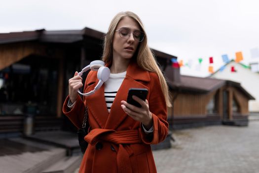 young stylish woman with headphones in her hands chooses a track on a mobile phone.
