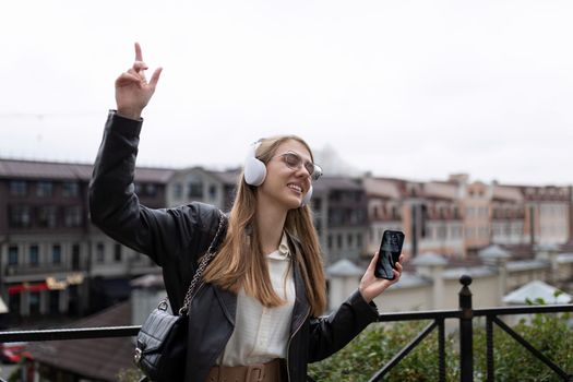 dancing young woman in headphones using a mobile phone against the backdrop of a city panorama.