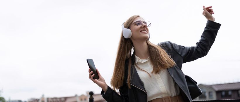 pretty with you a young woman with a mobile phone in her hands and headphones listens to music and dances against the backdrop of the city panorama.