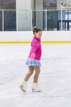 Little girl practicing figure skating on an indoor ice rink.