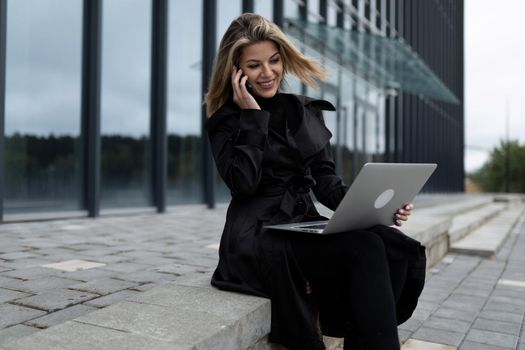 a middle-aged businesswoman woman works online on a laptop against the backdrop of an office building.