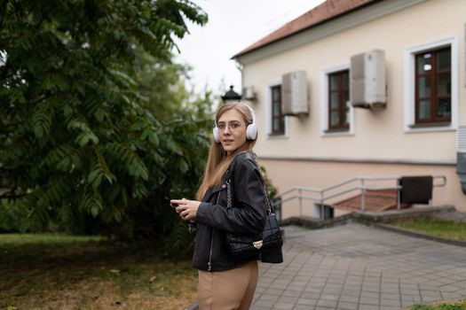 a young woman walks around the city listening to music on headphones and reading the news on her phone.
