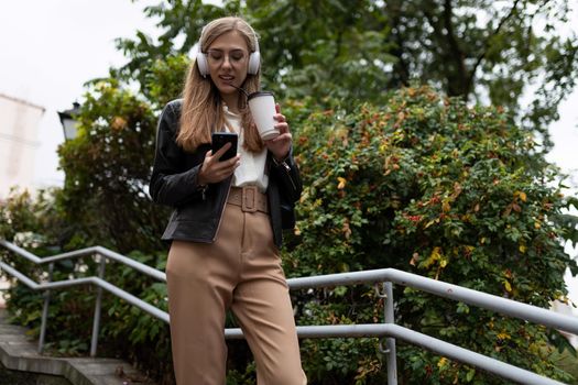 young woman in the city with a glass of coffee in headphones and a mobile phone.