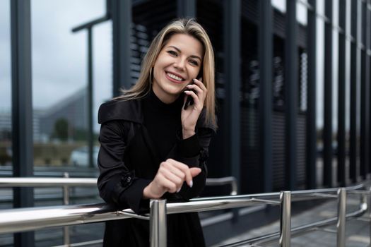 Business woman talking on a mobile phone with a smile looking at the camera on the background of a modern office building.