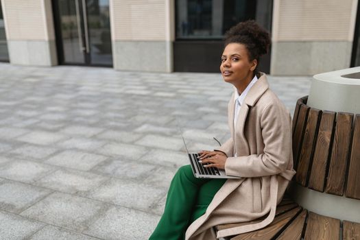 portrait of a successful young black woman with a laptop on a bench near the business center.