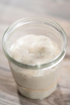 Feeding sourdough starter in a glass mason jar for baking artisan bread.