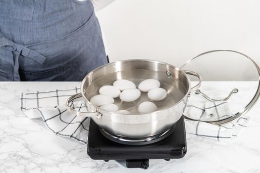 Boiling white eggs in a cooking pot to prepare hard-boiled eggs.