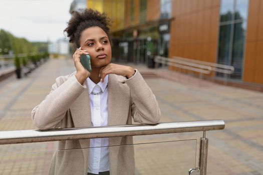 young African American serious woman talking on a mobile phone against the background of an administrative building.