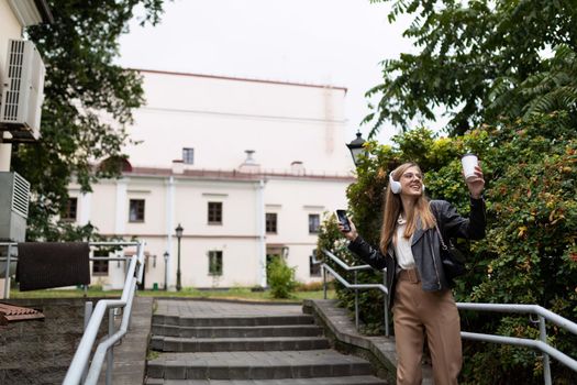 a young woman dances with headphones on the background of the urban environment without being shy.