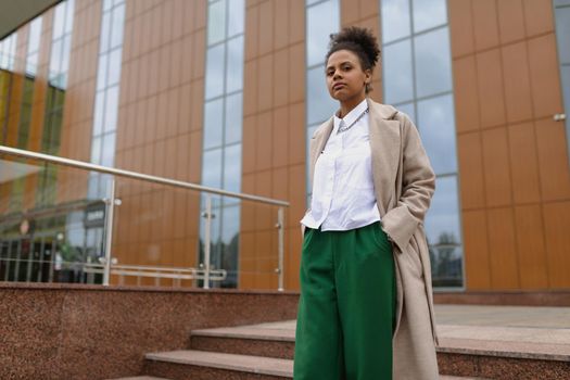 successful ambitious african american young woman with a serious face looks into the distance on the background of a city building.