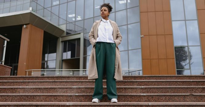 portrait of an African-American student in thought standing on the steps against the backdrop of an administrative city building.