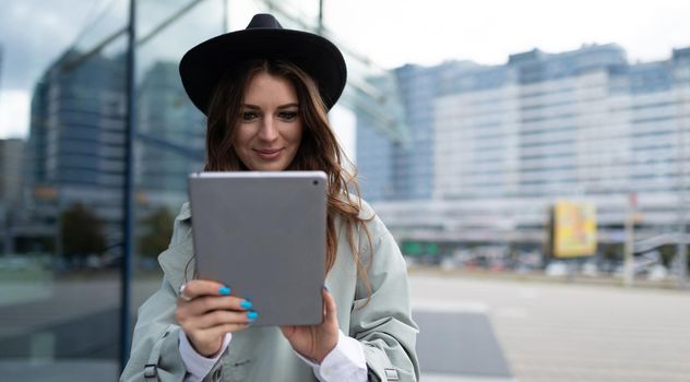 young woman working on a tablet online next to an office building in the city.