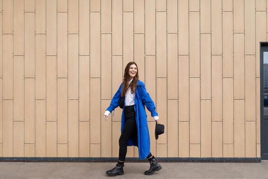 stylish woman in a blue autumn coat walks around the city against the background of a beige wall.