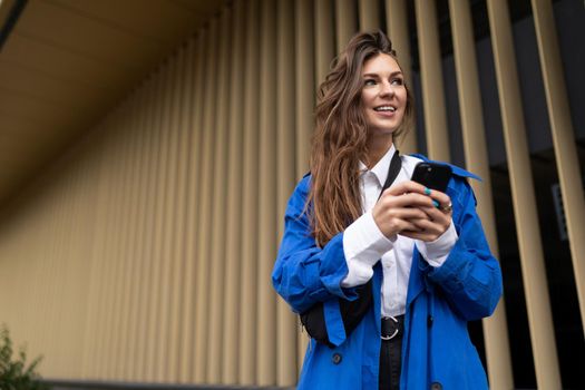 young female student with a mobile phone looking into the distance with a smile against the background of golden vertical stripes.