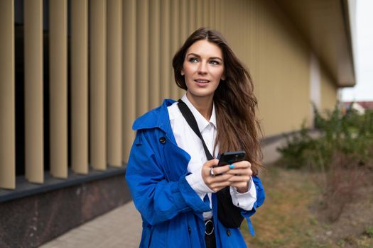 portrait of a beautiful young woman with a mobile phone in her hands against the backdrop of a modern city building.