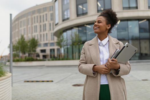 young satisfied african american woman walking around the city with a laptop and smiling.