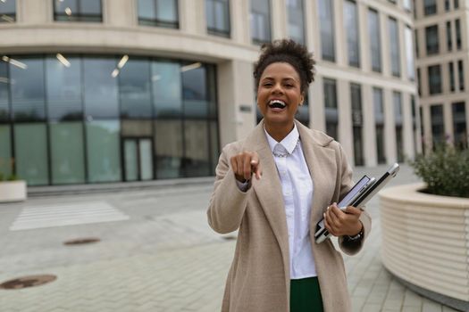 Satisfied woman businessman african american woman with joyful emotions points her finger forward with a wide smile.
