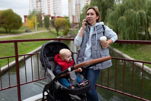 young woman talking on the phone while walking next to the stroller in which the baby is sitting.