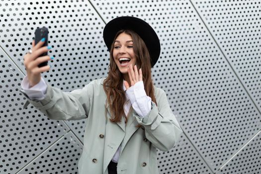 young woman emotionally talking on a video link of a mobile phone against the background of an aluminum facade of an office building.