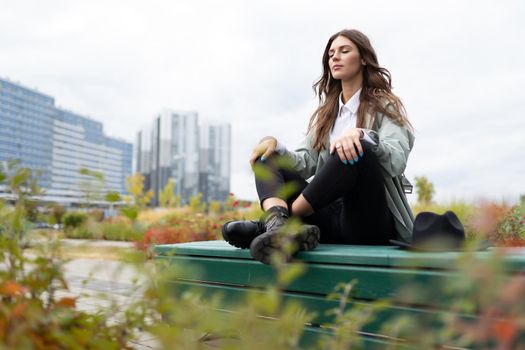 Meditation of an office employee on a park bench in a yoga position against the backdrop of office buildings.