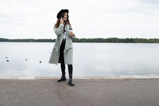 young stylish woman speaks on a mobile phone on the embankment against the background of the sea with a smile looks into the distance.