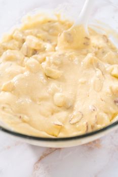 Mixing ingredients in a large glass mixing bowl to bake apple bundt cake with caramel glaze.