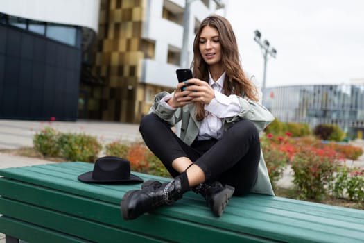 stylish young student sits on a bench in a yoga pose with a mobile phone on the background of the city.