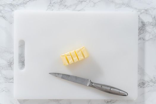 Flat lay. Slicing sticks of unsalted butter on a white cutting board.