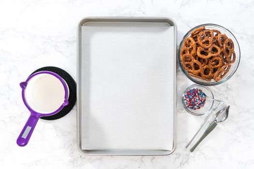 Flat lay. Dipping pretzels twists into melted chocolate to make red, white, and blue chocolate-covered pretzel twists.