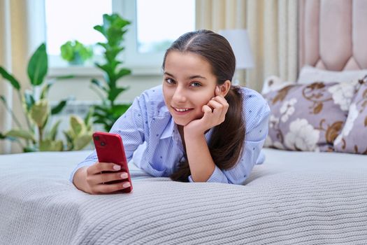 Young teenage female lying at home with smartphone, girl resting on bed using mobile apps. Lifestyle, technology, leisure, adolescence concept