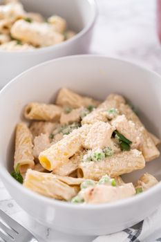 Chicken alfredo pasta with green peas and rigatoni pasta in a small bowl.
