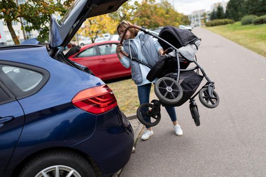 a young woman loads a stroller into the trunk of a car.