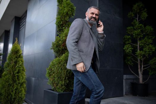 an elderly man businessman enters an office building talking on a mobile phone looking around with a smile.