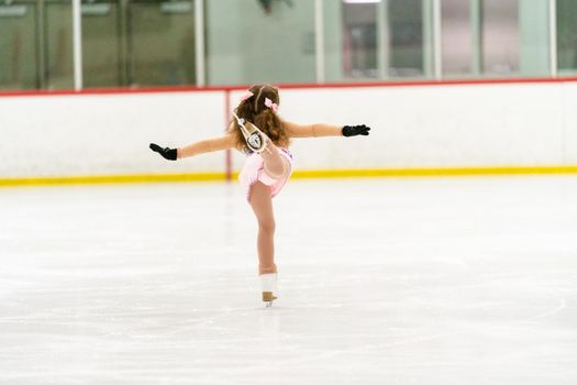 Little girl practicing figure skating on an indoor ice skating rink.