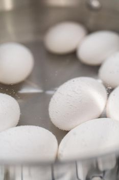 Boiling white eggs in a cooking pot to prepare hard-boiled eggs.