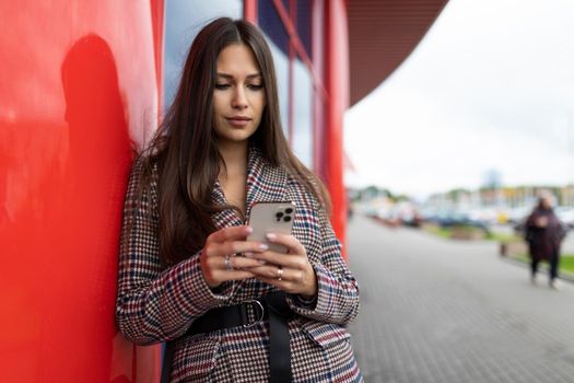 young business woman typing a message on the phone on the background of the red facade of the building.