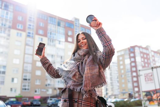 young successful satisfied with herself woman dancing listening to music in headphones from mobile phone on city panorama.