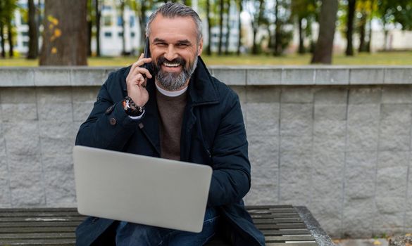 male businessman working on laptop Park talking on the phone smiling looking at camera.
