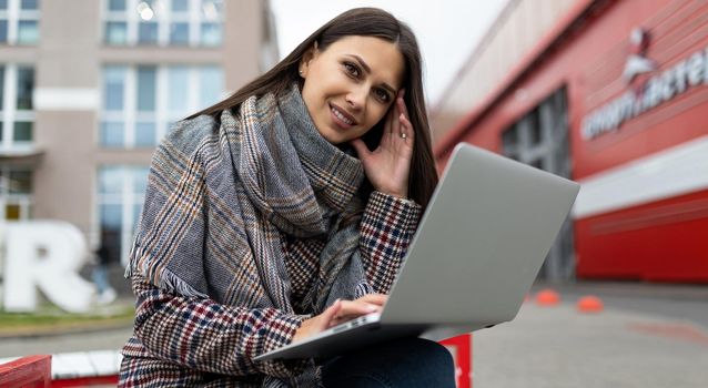 young beautiful woman in an autumn coat with a laptop on the background of city buildings.