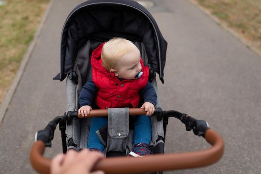 a small child with a pacifier in a baby carriage rides along the road.