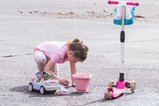 Little girl playing with chalk on a driveway in front of the house.