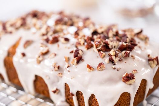 Glazing pumpkin bread with a white glaze and garnishing with shopped pecans.
