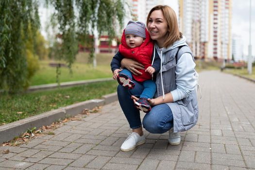 young mother sat down with a small child during a street walk with a smile looking at the camera.