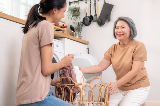 Daughter and mother working together to complete their household chores near the washing machine in a happy and contented manner. Mother and daughter doing the usual tasks in the house.