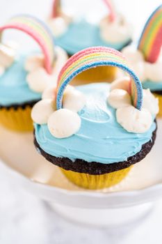 Chocolate cupcakes decorated with blue buttercream frosting and rainbow for unicorn theme birthday party.