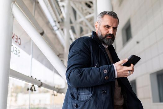 mature man waiting for boarding a flight at the airport looking at his mobile phone.